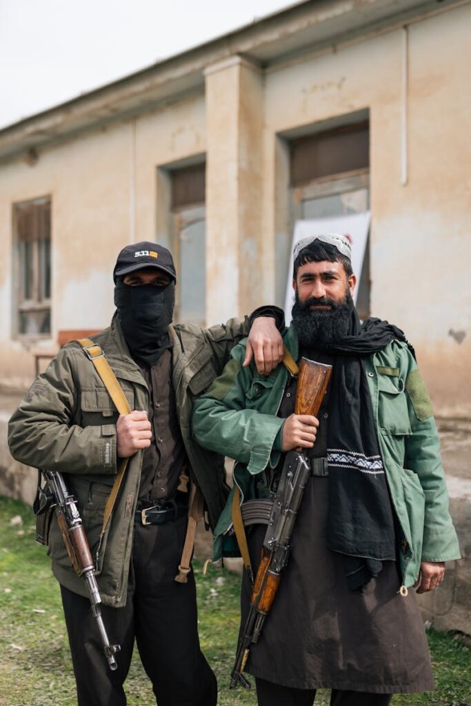 Two armed men pose in front of a building, showcasing traditional attire and weapons in Afghanistan.